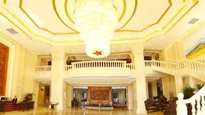 Eine geräumige Lobby mit einem prunkvollen Chandelier, einem Empfangstresen und einem Balkon.