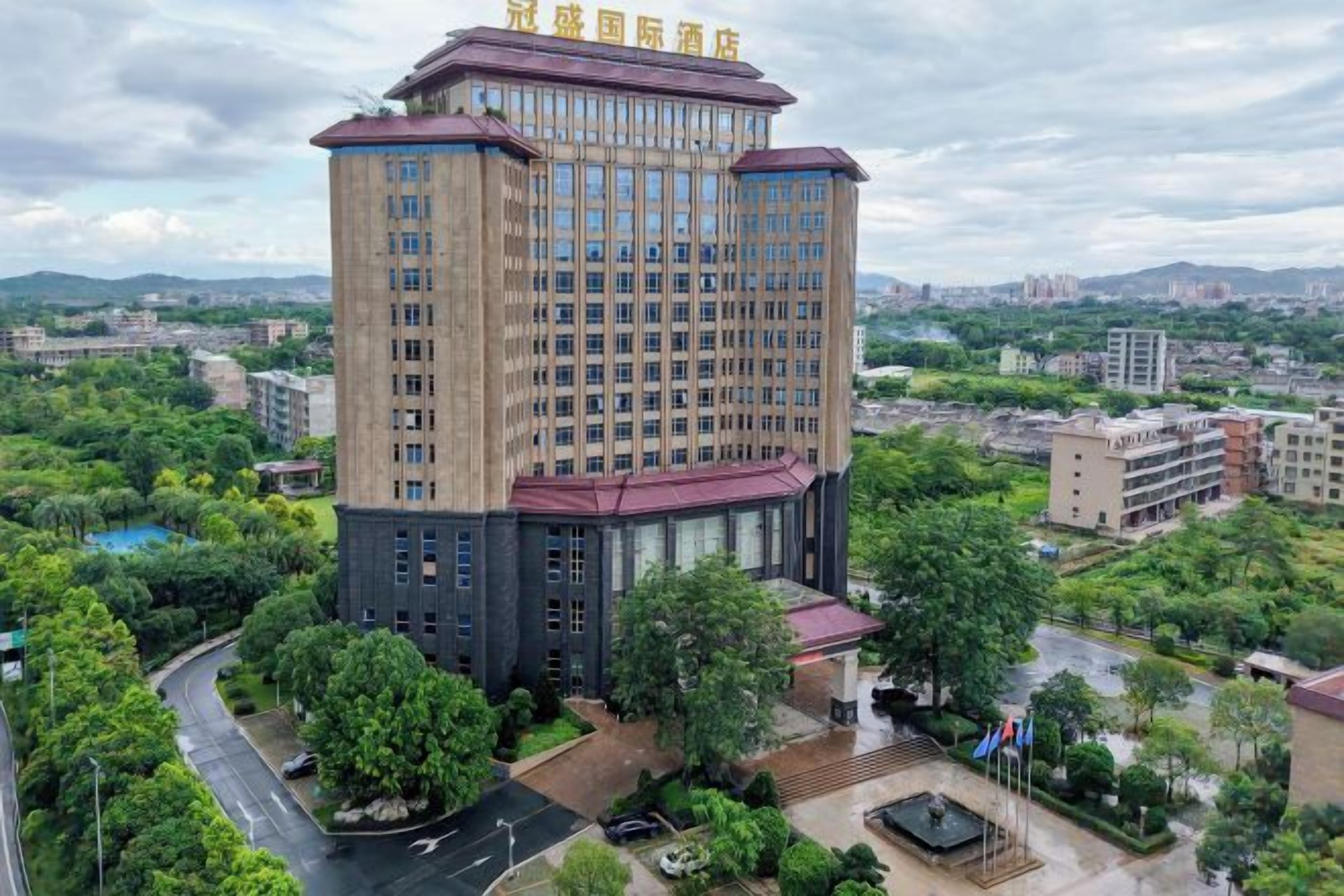 A multi-story hotel with a central courtyard, surrounded by greenery and other buildings.