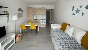 A modern, compact living space with a kitchenette, dining area, and a sofa with yellow cushions.