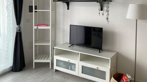 A modern living room with a TV on a white stand, black shelves above, and a wicker basket by the floor lamp.