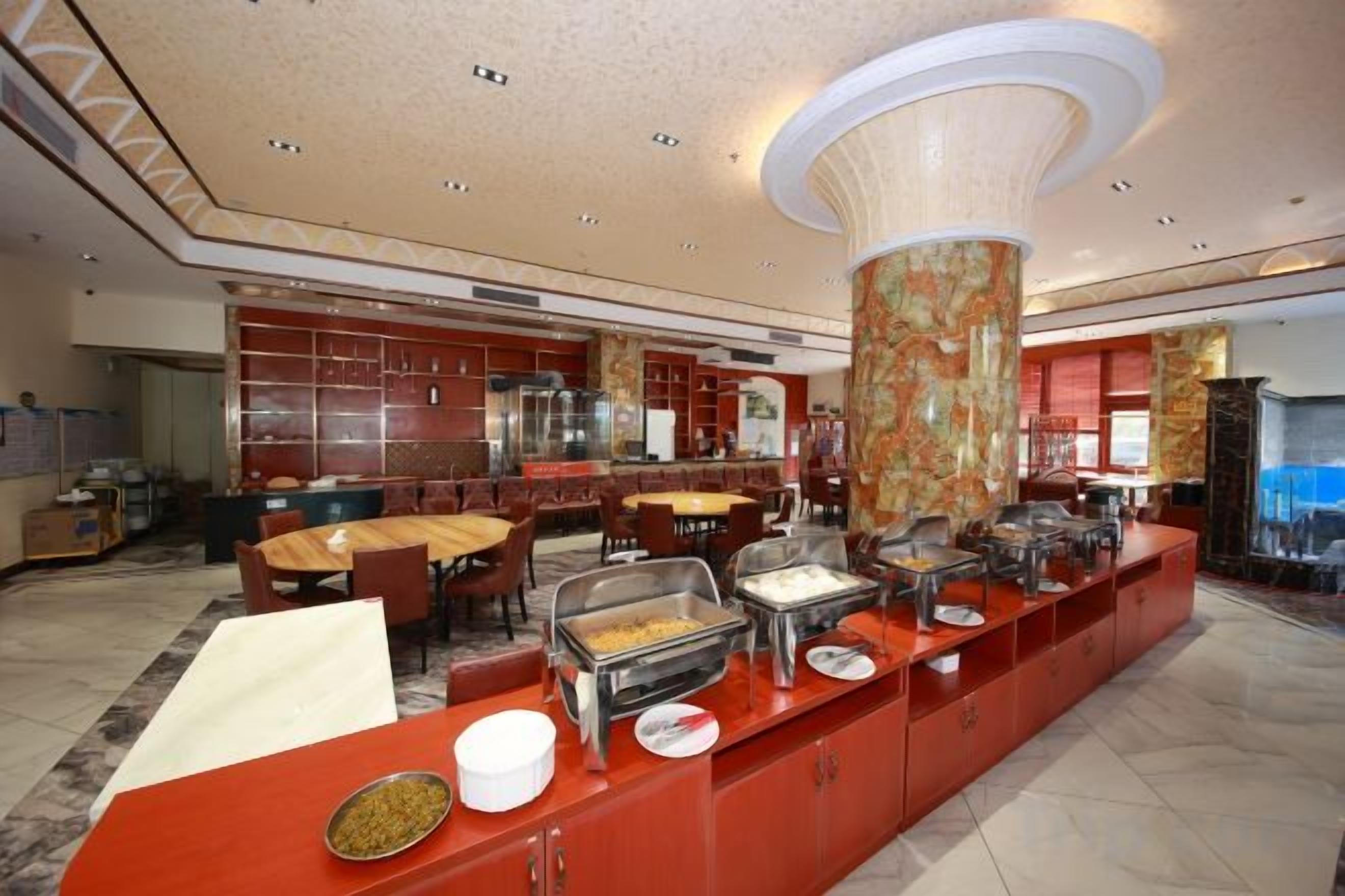 Un espace buffet doté de plusieurs points de service, d’une grande colonne centrale et d’un coin repas avec des tables et des chaises.