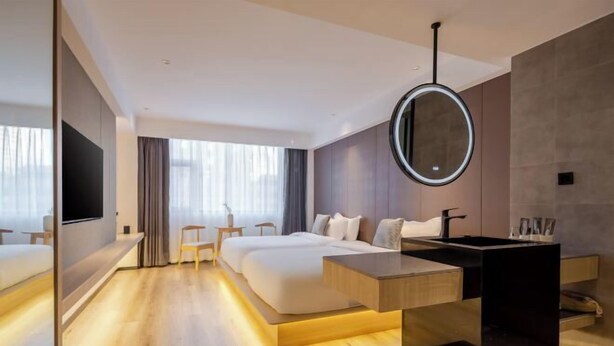 A modern hotel room with a large bed, bedside tables, a TV, and a bathroom with a mirror and sink. - Shenzhen Bolang Hotel (Xintangwei Metro Station) (Shenzhen)