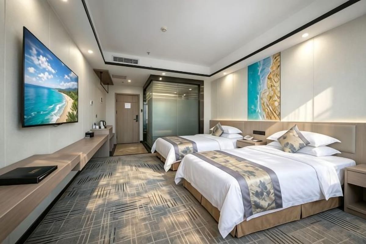 A hotel room with two beds, a flat-screen TV, a desk, and artwork on the walls.