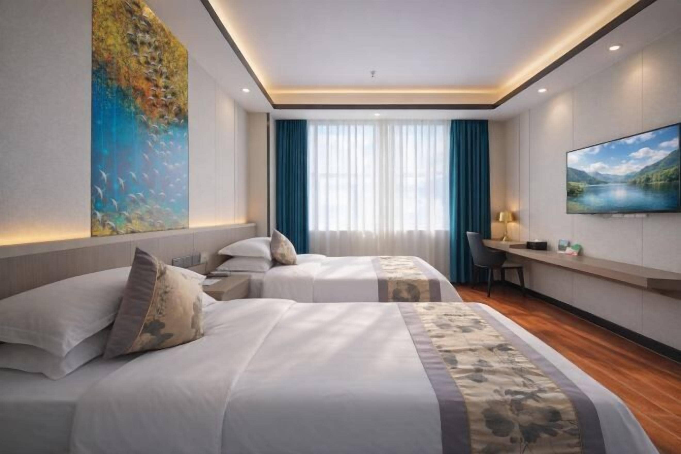 Quarto de hotel com duas camas, uma escrivaninha, uma televisão e um quadro grande na parede.