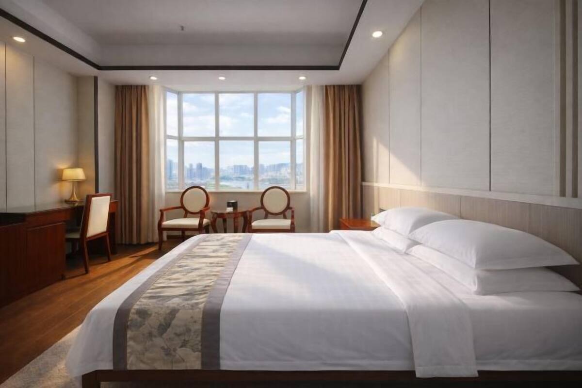 A hotel room with a large bed, two chairs, a desk, and a view of the city.