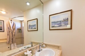 A bathroom with a large mirror, a sink, and a robe hanging on the wall.
