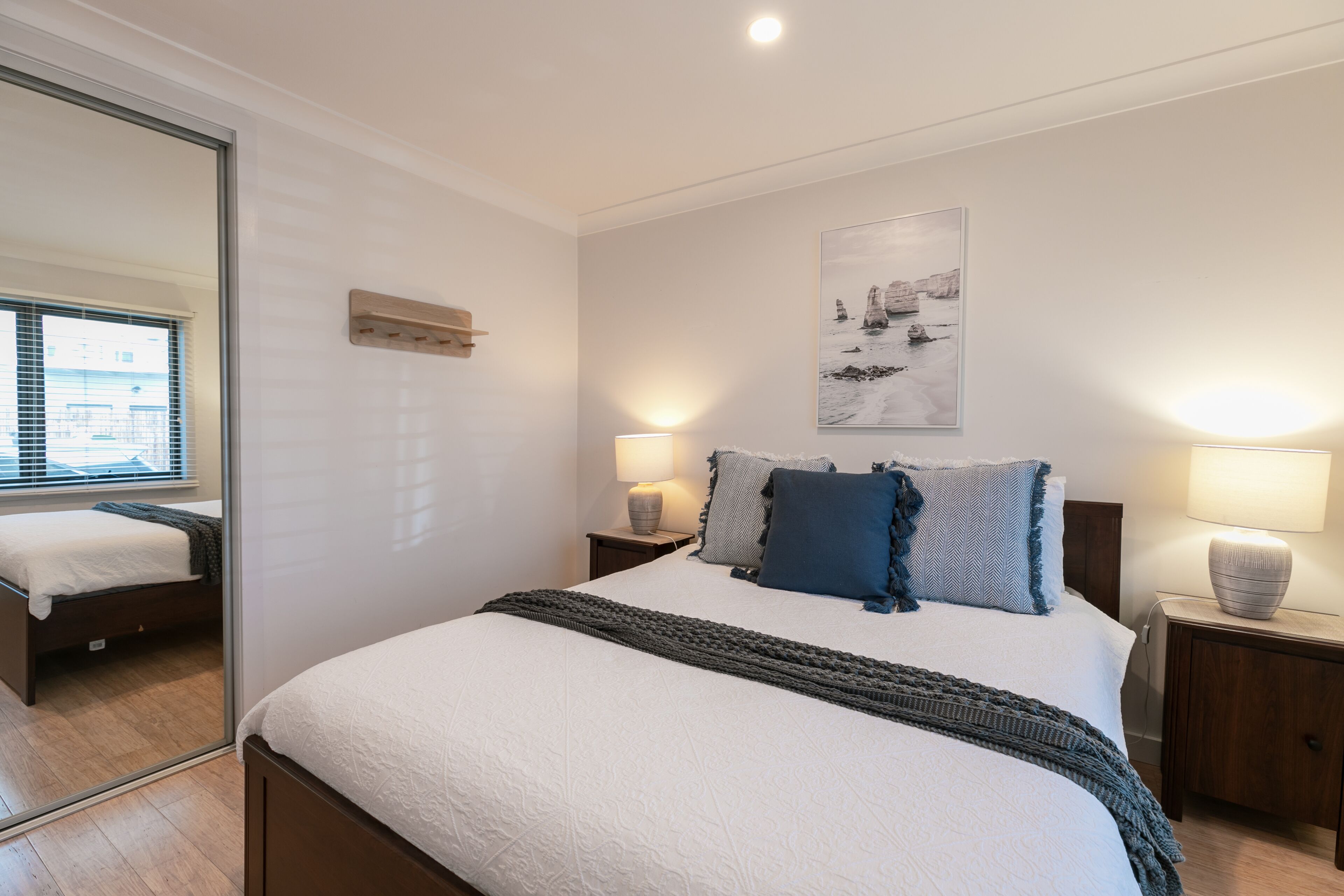A bedroom with a large bed, two bedside tables with lamps, a mirror, and a wall-mounted shelf.