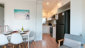 Une cuisine moderne avec des meubles blancs, un réfrigérateur noir et un coin repas comprenant une table et des chaises blanches.