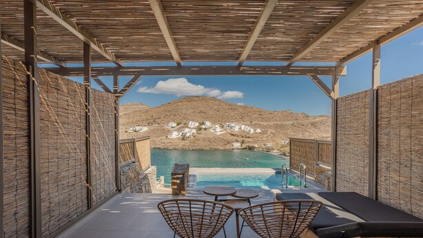 A covered outdoor seating area with a pool, overlooking a mountainous landscape and a coastal town.