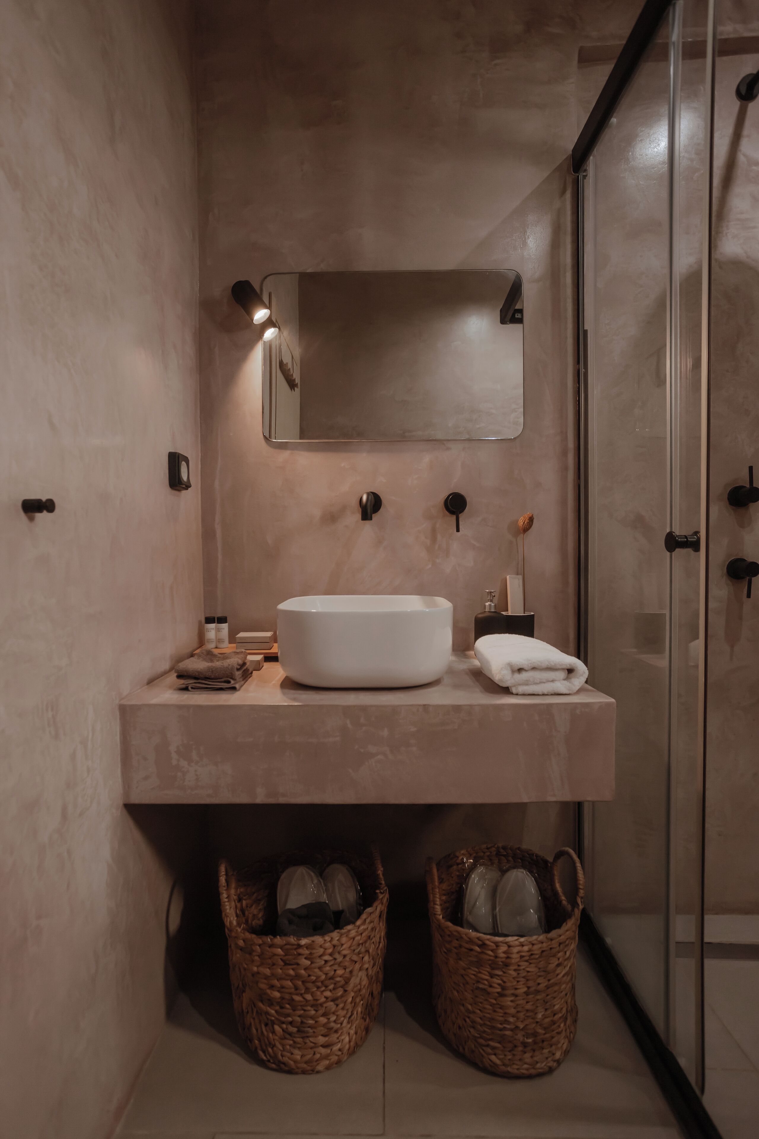 Un baño moderno con un lavamanos grande de color blanco, un espejo encima y dos cestas de mimbre debajo.