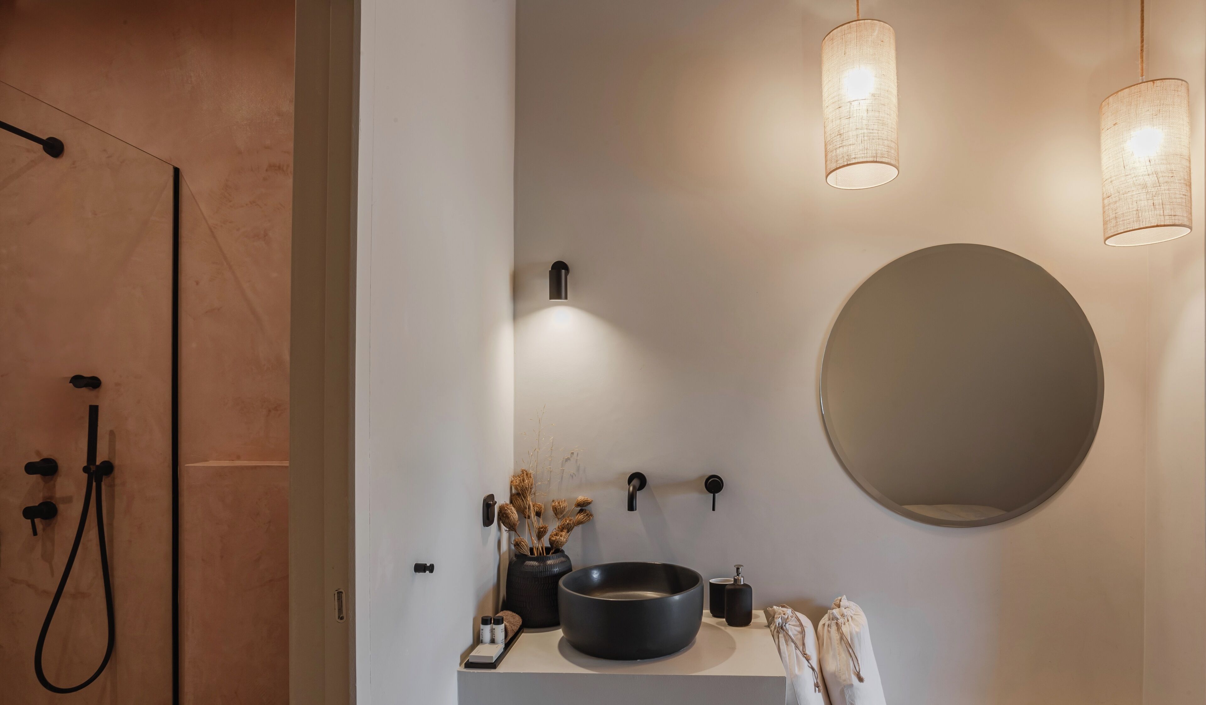 A modern bathroom with a round mirror, a black sink, and two pendant lights.