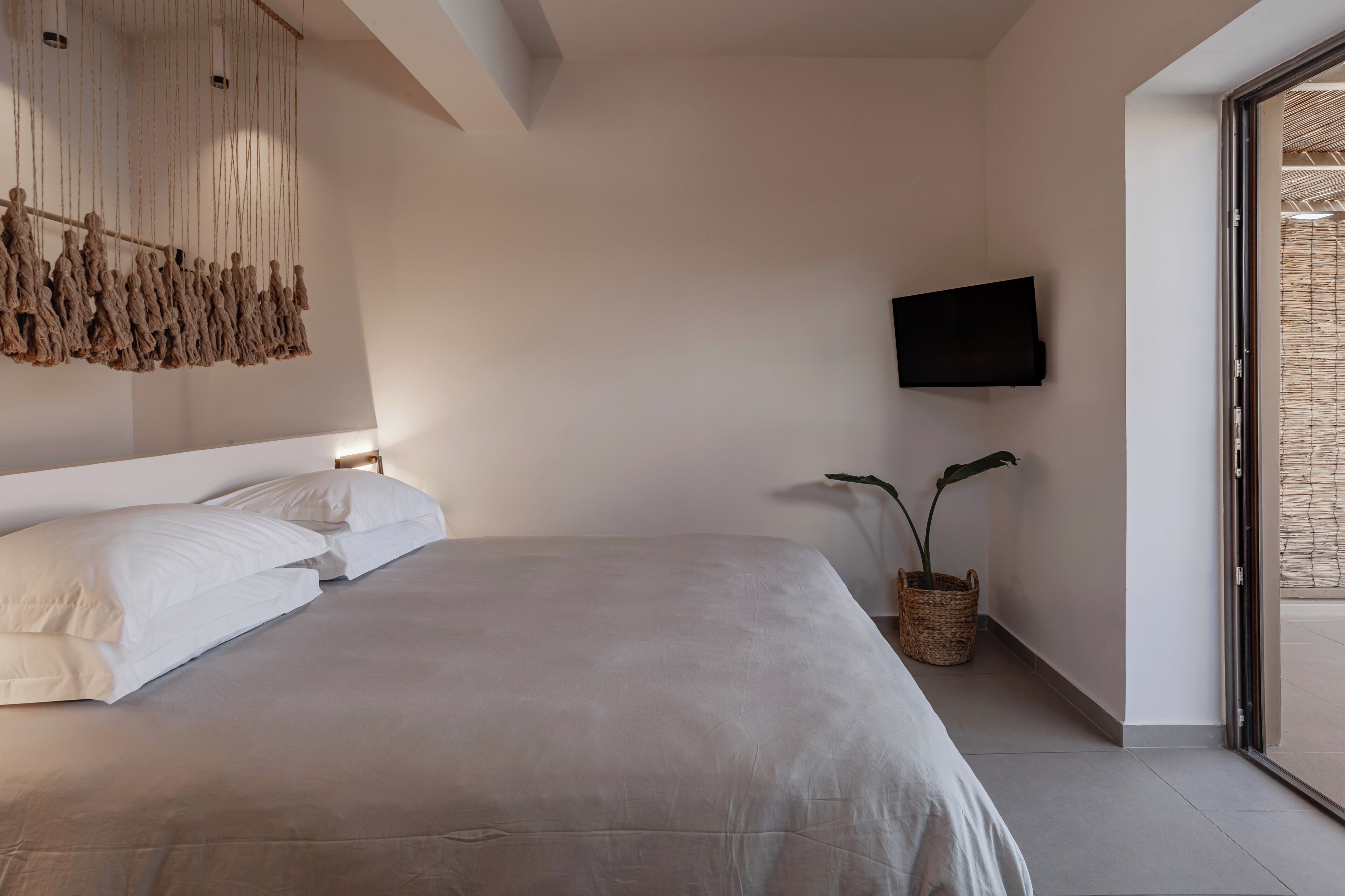 Un dormitorio moderno con una cama grande, un televisor de pantalla plana montado en la pared y una planta en maceta.