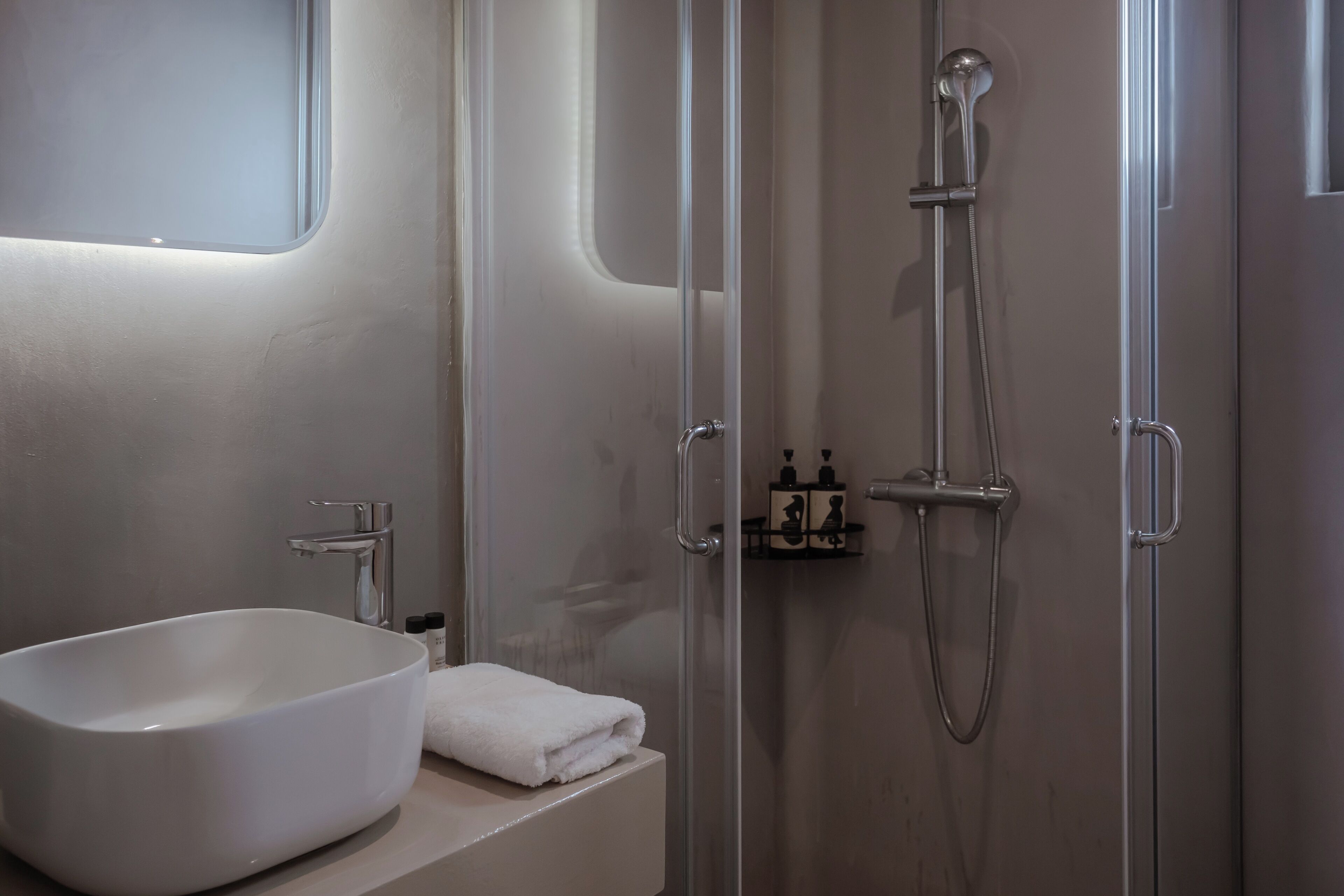 A modern bathroom with a large white sink, a glass-enclosed shower, and a small shelf with toiletries.