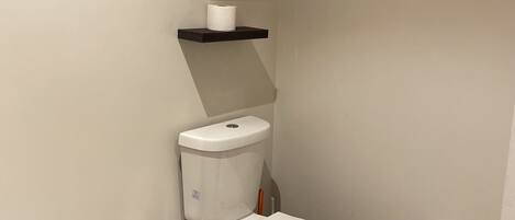 A modern bathroom with a toilet, a trash can, and two shelves with toilet paper.