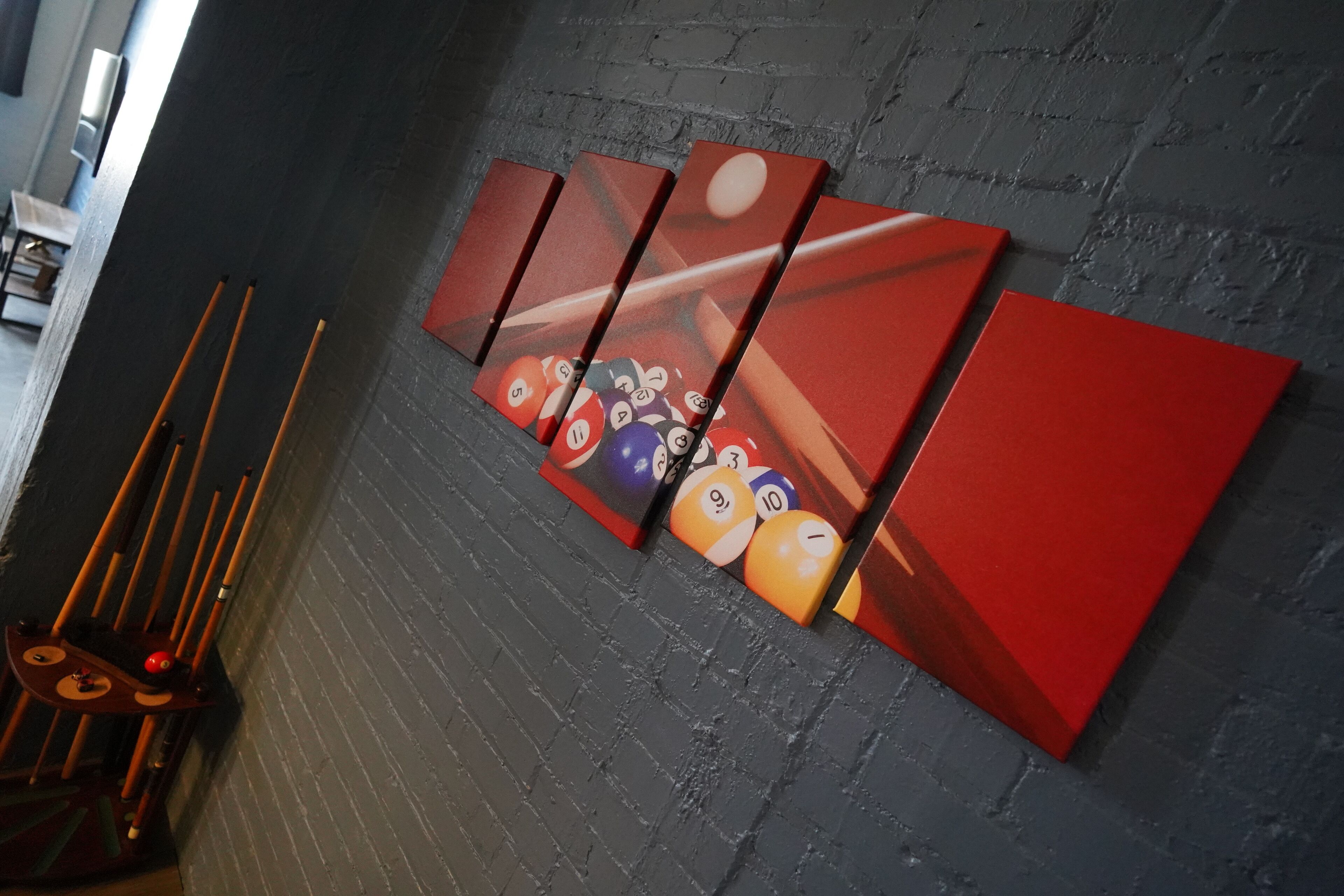 Una mesa de billar con un juego de tacos y una pared roja con diseño de bolas de billar.