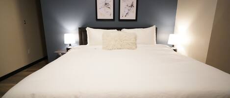 A neatly made bed with white bedding and a fluffy pillow in a room with dark blue walls.