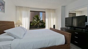 A hotel room with a large bed, a TV, a dresser, and a window with curtains.