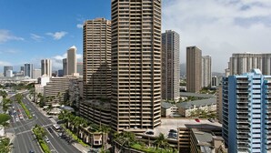 A high-rise building with multiple floors and balconies, surrounded by other tall buildings and a busy road with palm trees.