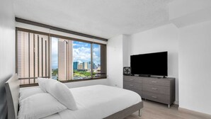 A modern bedroom with a large window, a bed, a TV, and a dresser. - Monthly Discovery Bay 1902 2 Bd  Ocean Views/ High Floor / 2x Queen Beds+Sofa Bed (Honolulu)