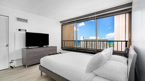 A modern hotel room with a large bed, a flat-screen TV, a dresser, and a balcony with a city view. - Monthly Discovery Bay 1902 2 Bd  Ocean Views/ High Floor / 2x Queen Beds+Sofa Bed (Honolulu)