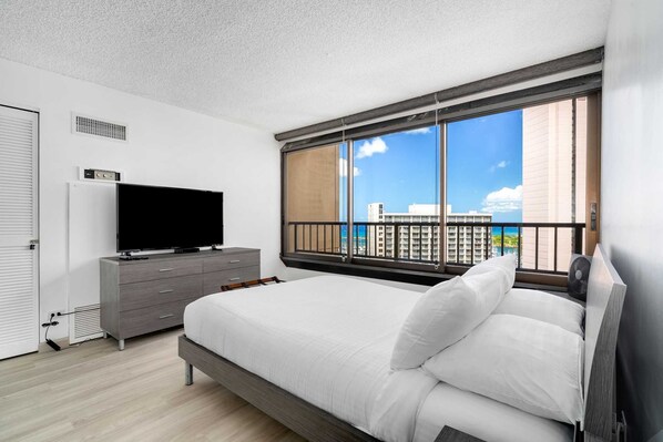 A modern hotel room with a large bed, a flat-screen TV, a dresser, and a balcony with a city view.