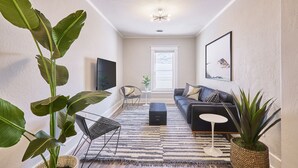 Un salon moderne avec un canapé noir, une table basse et de grandes plantes vertes.