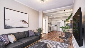 Un salon moderne avec un canapé en cuir noir, un grand tableau abstrait et un coin repas comprenant une table et des chaises.
