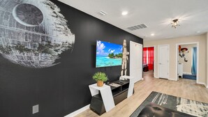 A modern living room with a large wall mural, a flat-screen TV, a black leather sofa, and a wooden floor. - Private Conservation View With Theme Rooms and Beautiful Pool Area, Perfect for Families #5st4591 (Davenport)