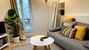 A living room with a grey sofa, yellow cushions, a white coffee table, and a potted plant. - 1 Bedroom Apartment in Paris (Paris)