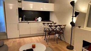 A compact kitchen with a dining area, including a table with chairs, a coffee maker, and a remote control on the table. - 1 Bedroom Apartment in Paris (Paris)