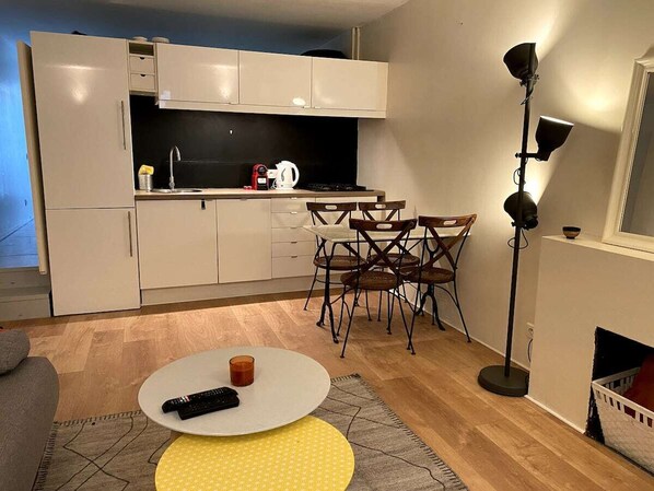 A compact kitchen with a dining area, including a table with chairs, a coffee maker, and a remote control on the table. - 1-Bedroom Apartment in Paris (Paris)