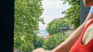 A person in a red shirt leaning on a window with a view of a cityscape, including trees, a bridge, and a body of water. - RW Boutique Hotel (Istanbul)
