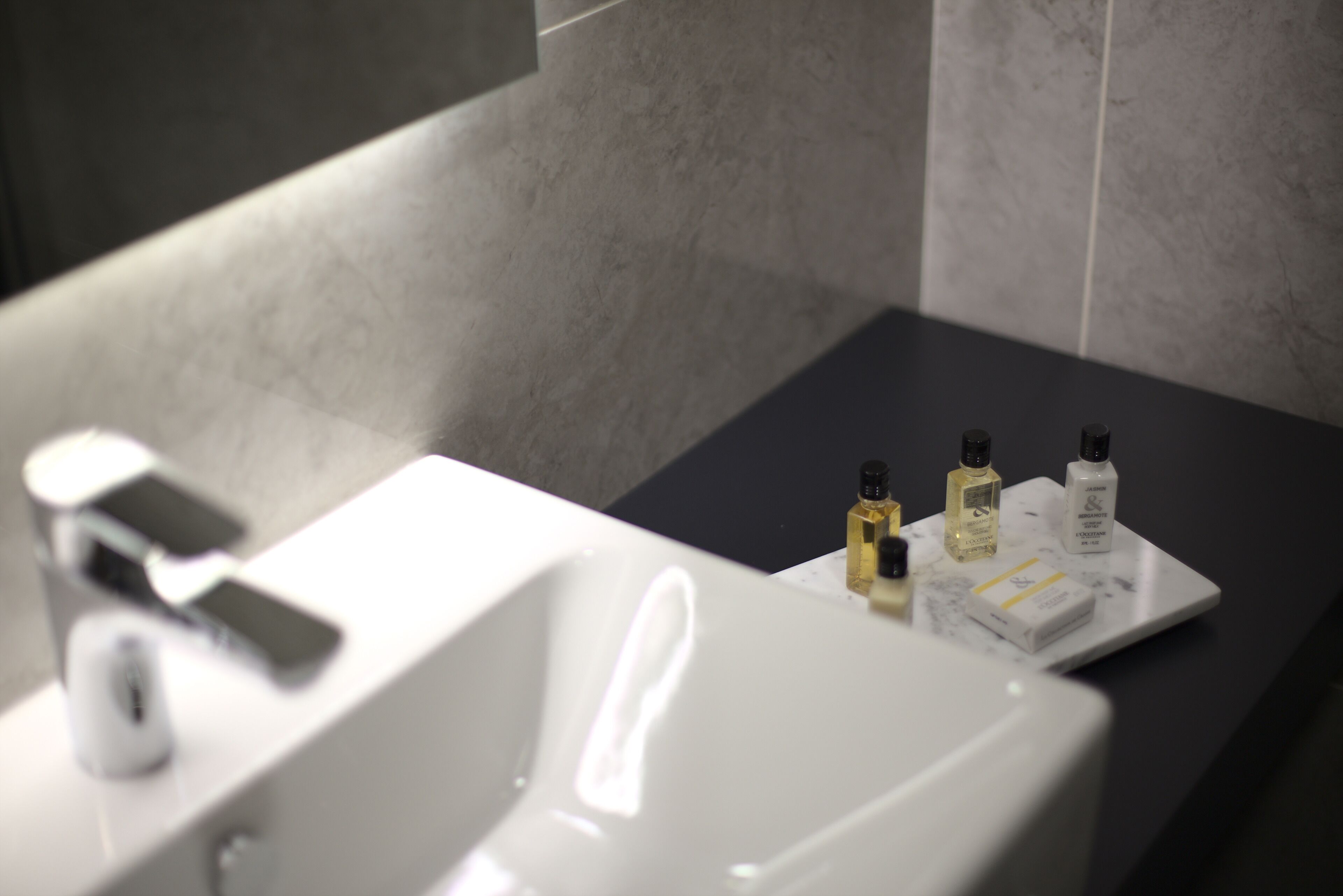 A modern bathroom with a white sink, a black countertop, and several toiletries.