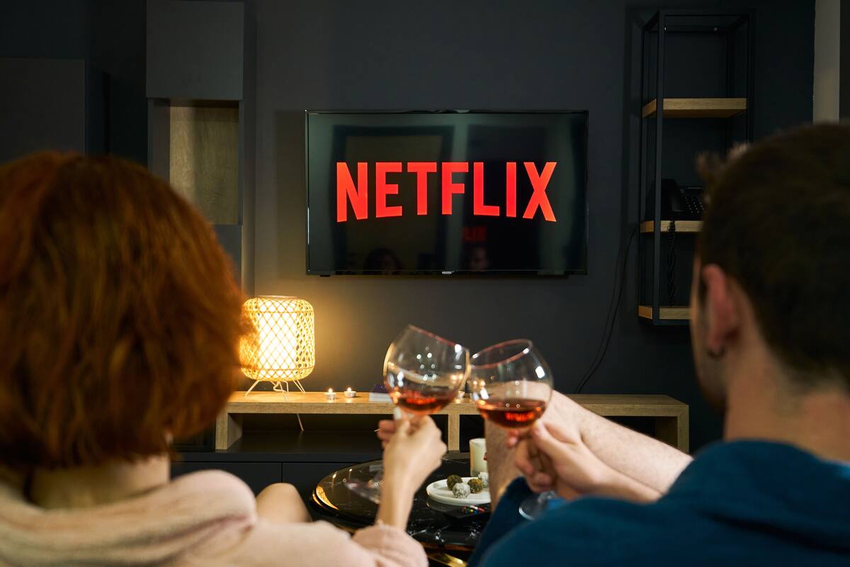 A room with a television displaying the Netflix logo, a table with a candle, and two people holding wine glasses.