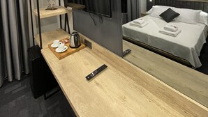 A modern hotel room with a wooden desk, a flat-screen TV mounted on the wall, a bed with white linens, and a large mirror reflecting the room. - RW Boutique Hotel (Istanbul)