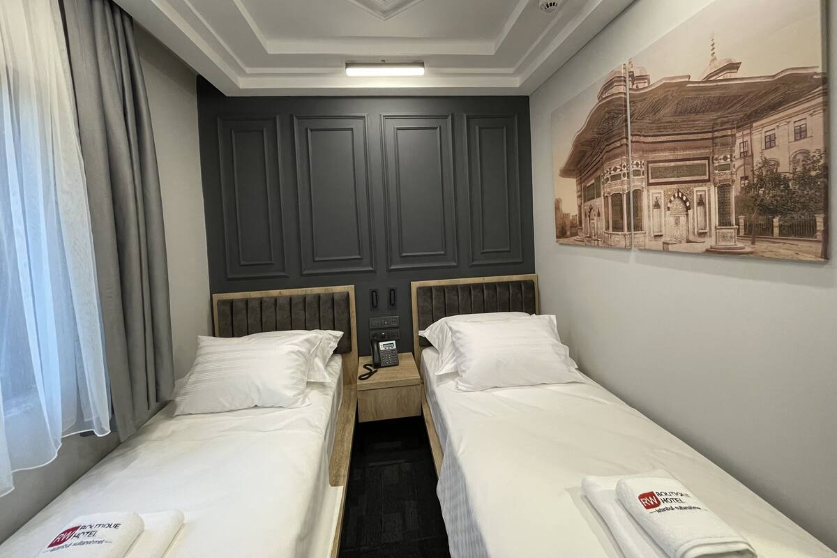 A hotel room with two beds, a painting on the wall, and a curtain.