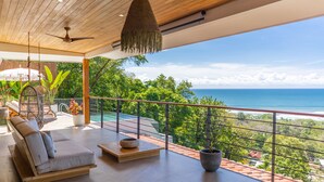 Ein moderner Balkon mit einer Couch, einem Hängestuhl und Pflanzen in Töpfen.