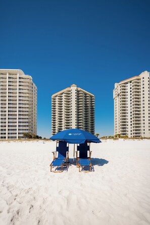Una playa con dos edificios altos, una sombrilla azul y una silla de playa.