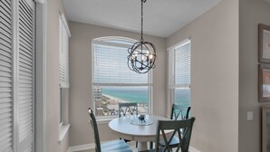 A dining area with a round table and two chairs, large windows with beach views, and a hanging light fixture. - Beach Colony East 15A- 3BD/3BA Gulf front w/Beach Service & Onsite Management (Navarre Beach)