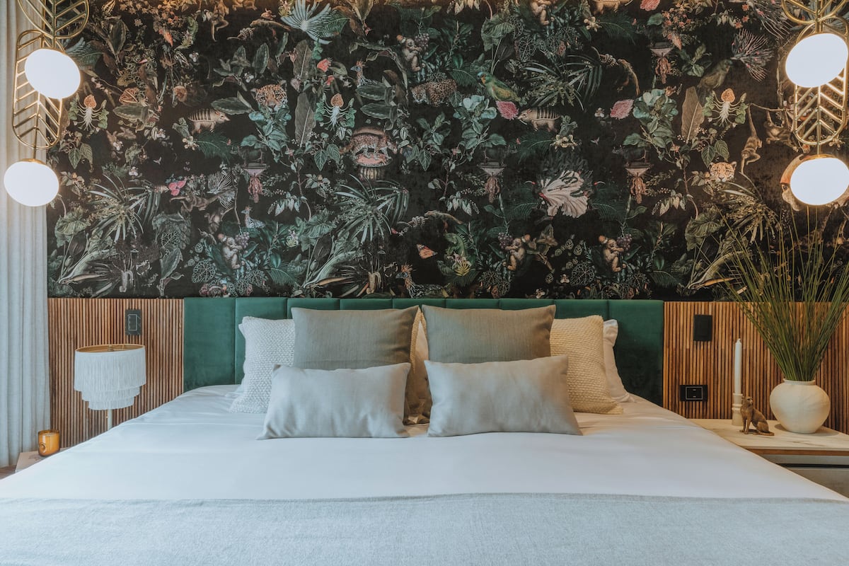 Une chambre avec un grand lit, une tête de lit verte et une fresque murale représentant des plantes tropicales.