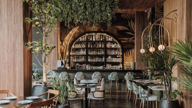 Eine Bar mit Holzbalkendecke, Flaschenregalen und Tischen mit Stühlen.