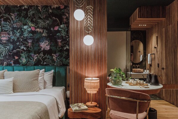 A bedroom with a green upholstered headboard, a bedside table with a lamp, and a small round table with a plant and a book. - Selvario 36 Hotel (Medellín)