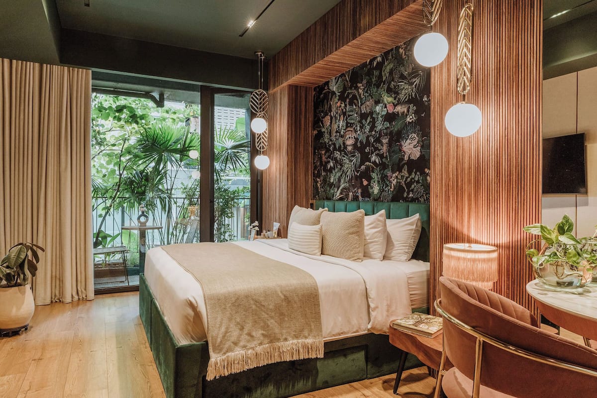 Une chambre moderne avec un grand lit, une tête de lit verte et une vue sur la verdure environnante.