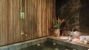 Ein Wellnessbereich mit einer Holzwand, einer Steinwand, einem kleinen Pool und einem Handtuch auf einer Holzliege.