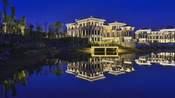 A waterfront property with multiple buildings, a reflective pool, and surrounding trees. - Lotus Villa Hotel (Liuzhou)