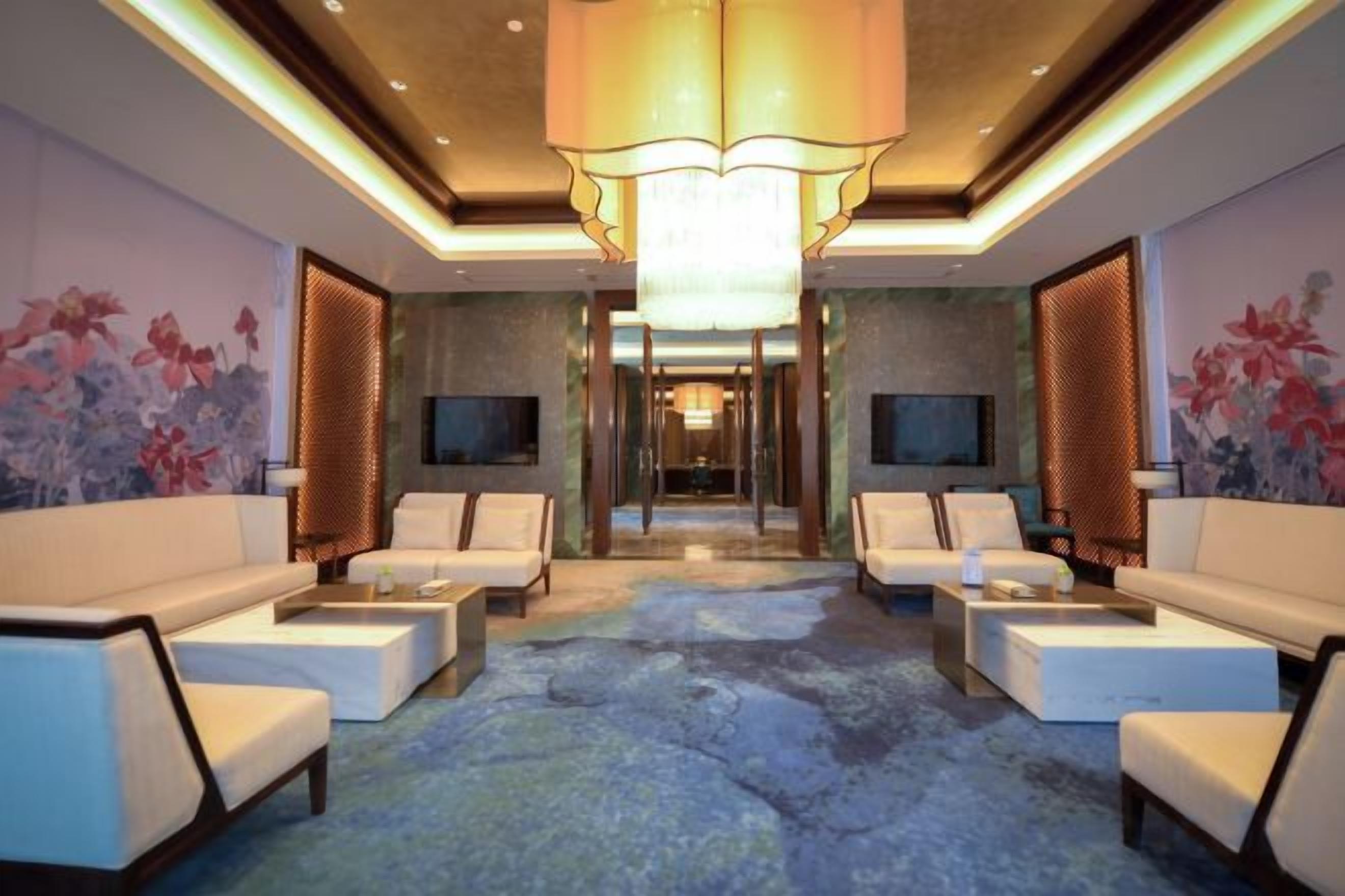 A hotel lobby with a central seating area, a chandelier, and a television on the wall.