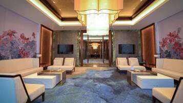 A hotel lobby with a central seating area, a chandelier, and a television on the wall.