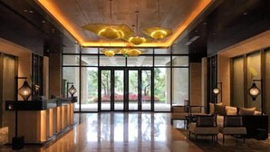 A modern lobby with a reception desk, seating area, and large windows offering a view of greenery. - Lotus Villa Hotel (Liuzhou)