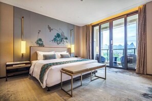 Ein modernes Hotelzimmer mit einem großen Bett, einer Bank, einem Nachttisch und Blick ins Freie durch große Fenster.