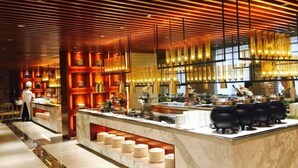 A modern hotel lobby with a marble reception desk, a chef preparing food, and a warm, wooden ceiling with hanging lights. - Lotus Villa Hotel (Liuzhou)